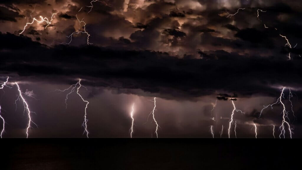 Multiple lightning bolts striking beneath dark thunderstorm clouds.