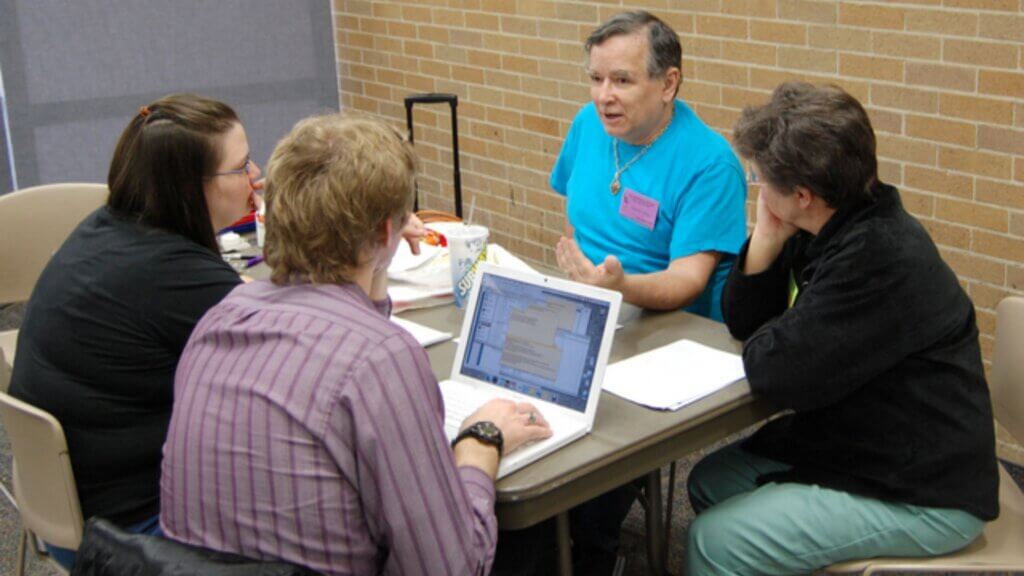 Group of adults seated at a table discussing with a laptop during a meeting.