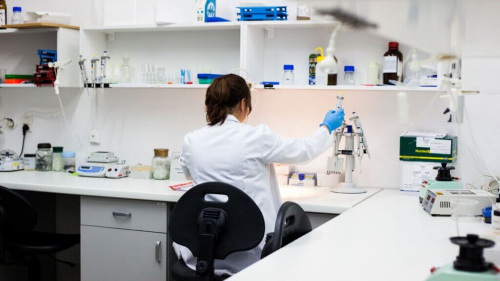 Scientist in lab coat using pipette to handle samples at a laboratory workstation.