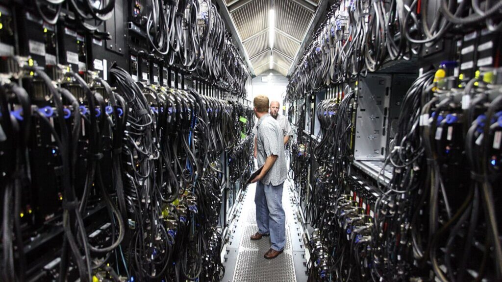 Workers standing between rows of servers inside a data center.