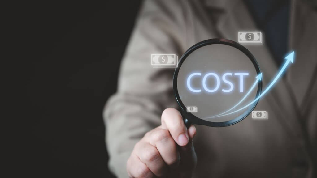 Business professional holding a magnifying glass over the word cost with financial icons and an upward arrow