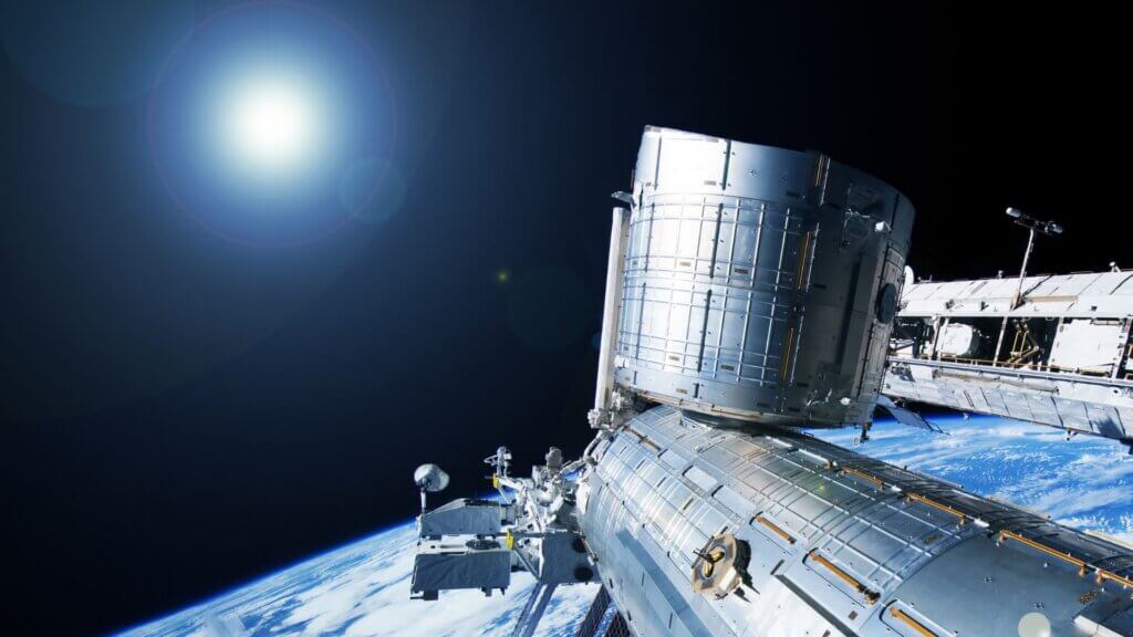 International Space Station orbiting Earth with sun flare visible in space.