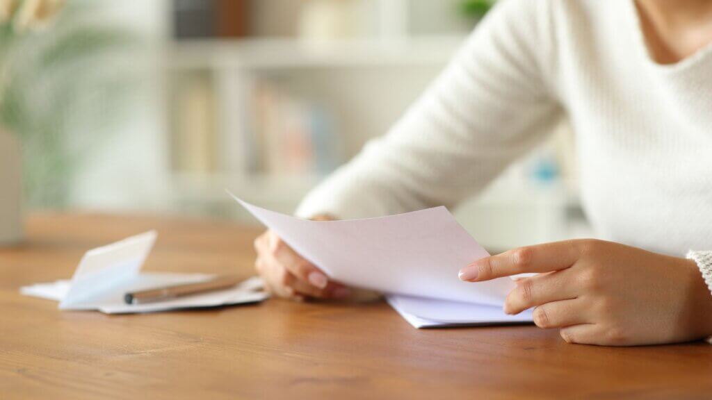 Person holding and reading a letter while seated at a table indoors.
