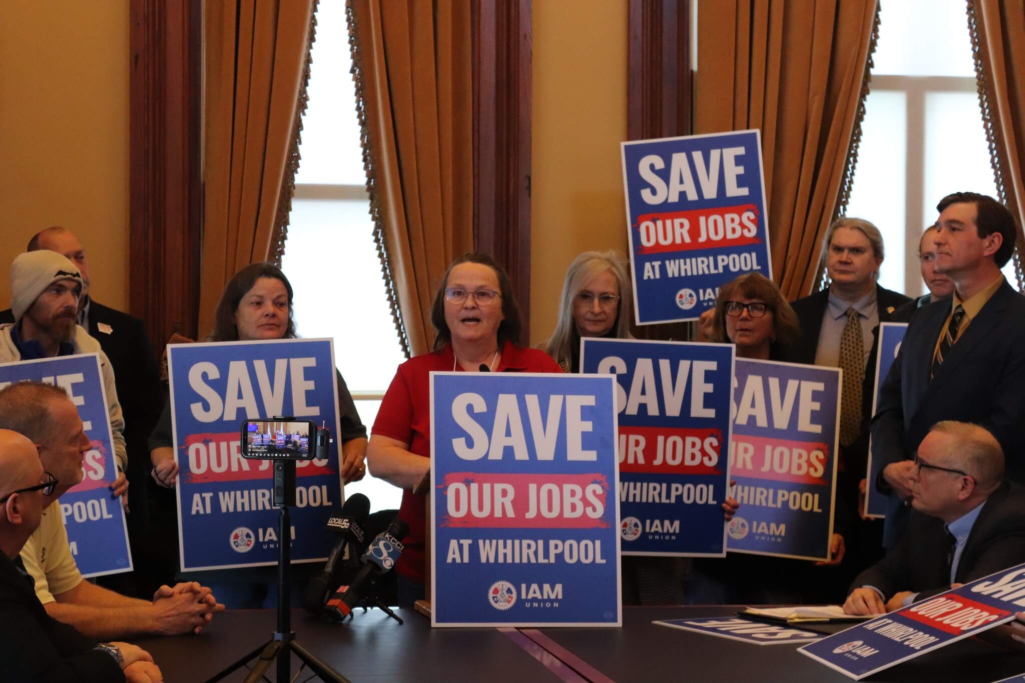 Whirlpool workers and union members hold “Save Our Jobs at Whirlpool” signs during a press conference about layoffs at the Iowa plant.