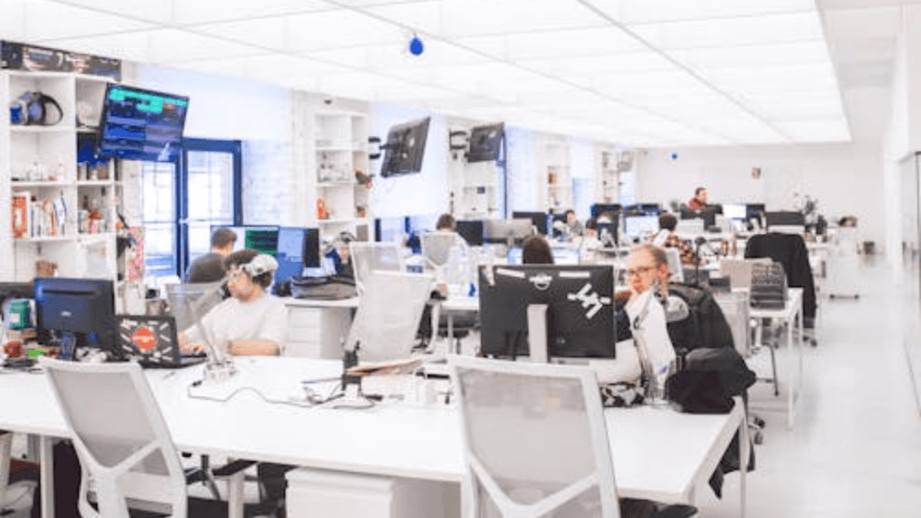 People sit at white desks and work on computers in a bright office.