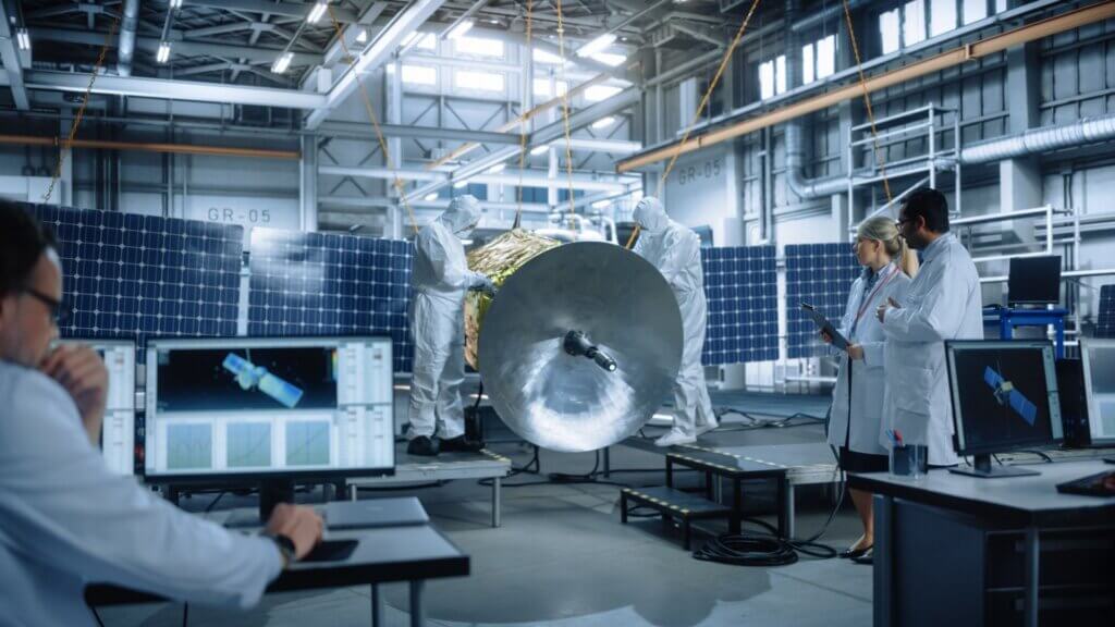 Engineers in cleanroom assembling and inspecting a satellite with solar panels.