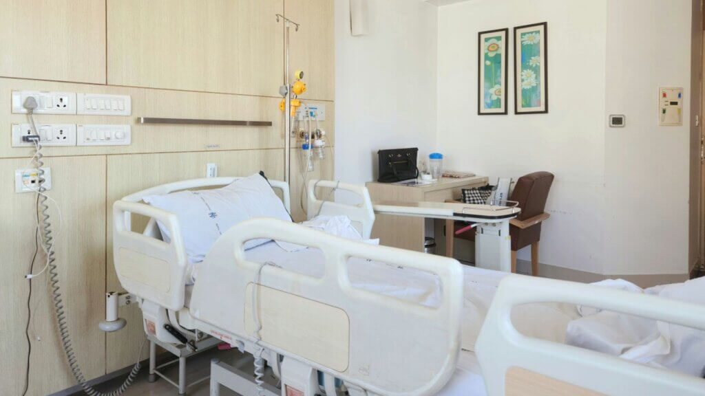 Hospital room with a patient bed, medical equipment, and a desk area.