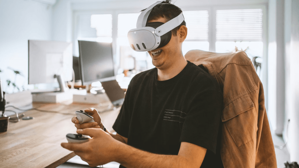 A smiling man wears a white virtual reality headset and holds two controllers.