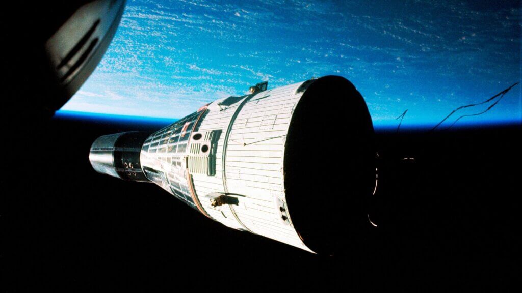 Historic spacecraft orbiting Earth with cylindrical module and planet horizon visible.