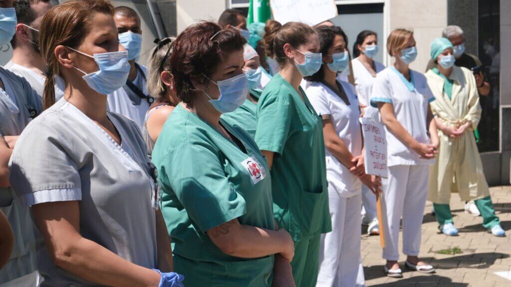 Healthcare workers wearing masks standing together outside a hospital building.