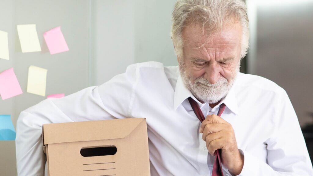 Senior office employee holding a box of belongings after losing a job and leaving the workplace