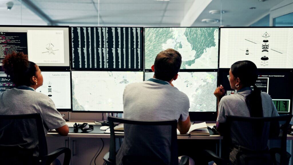 Team analyzing satellite data on multiple screens displaying maps and telemetry.