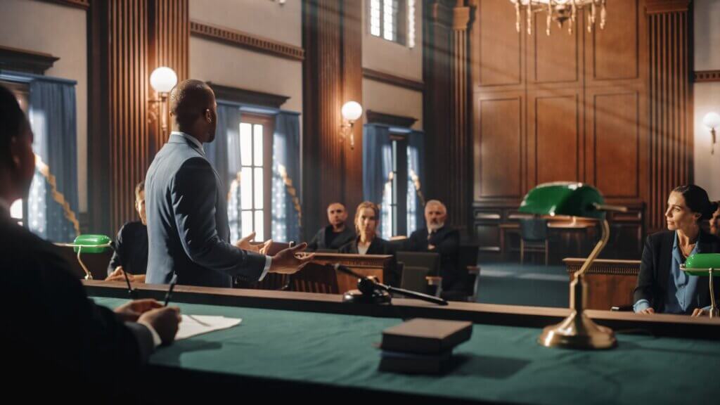 Man speaking in a courtroom with judge and attendees listening during proceedings.