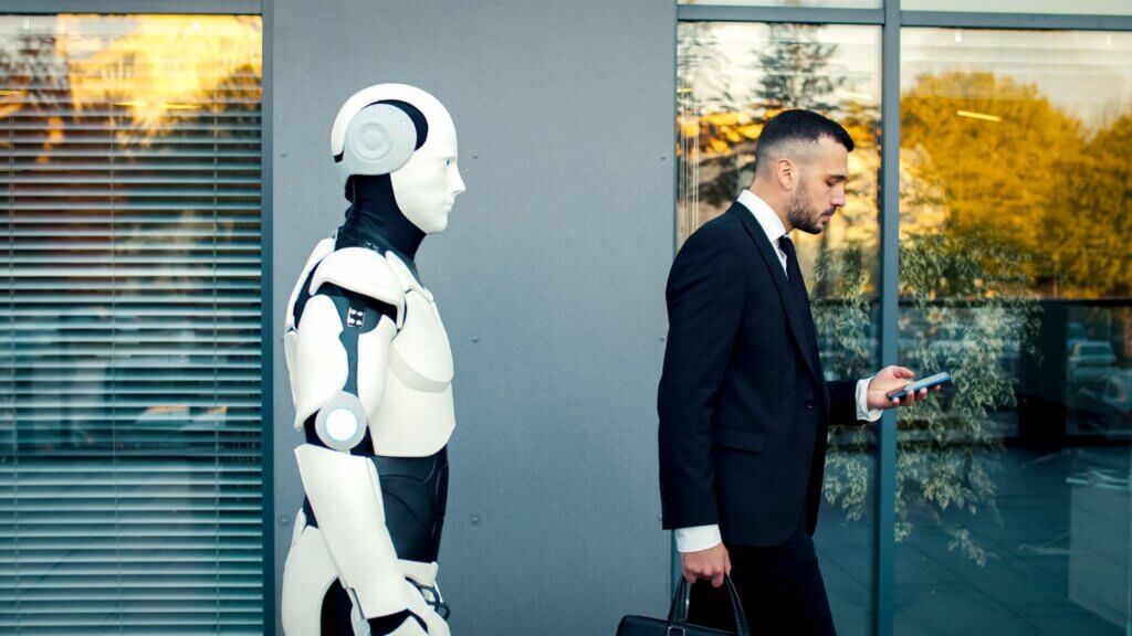 Robot standing near a businessman walking while looking at his phone outside a modern office building