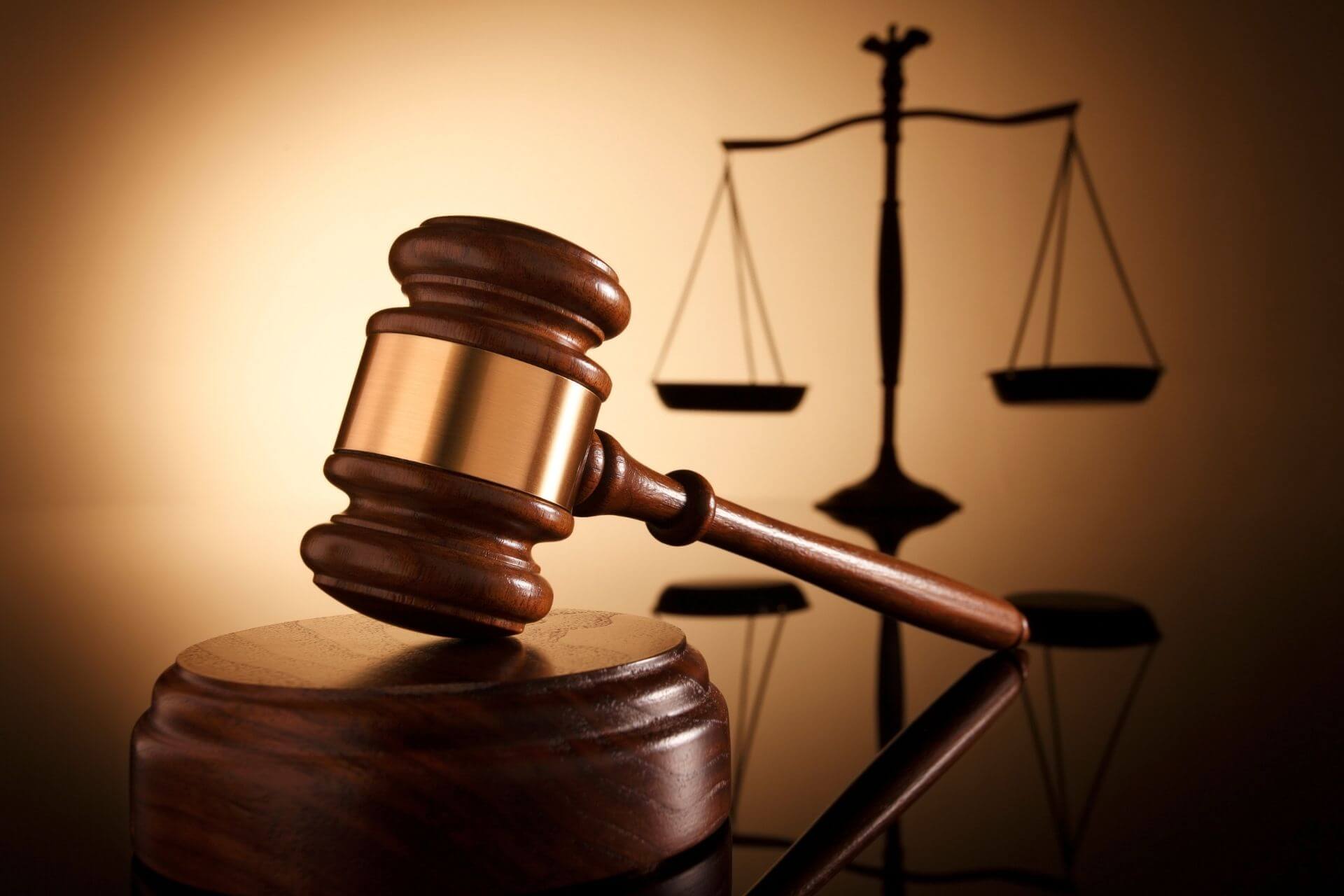 Judge’s gavel resting on a block with scales of justice in the background.