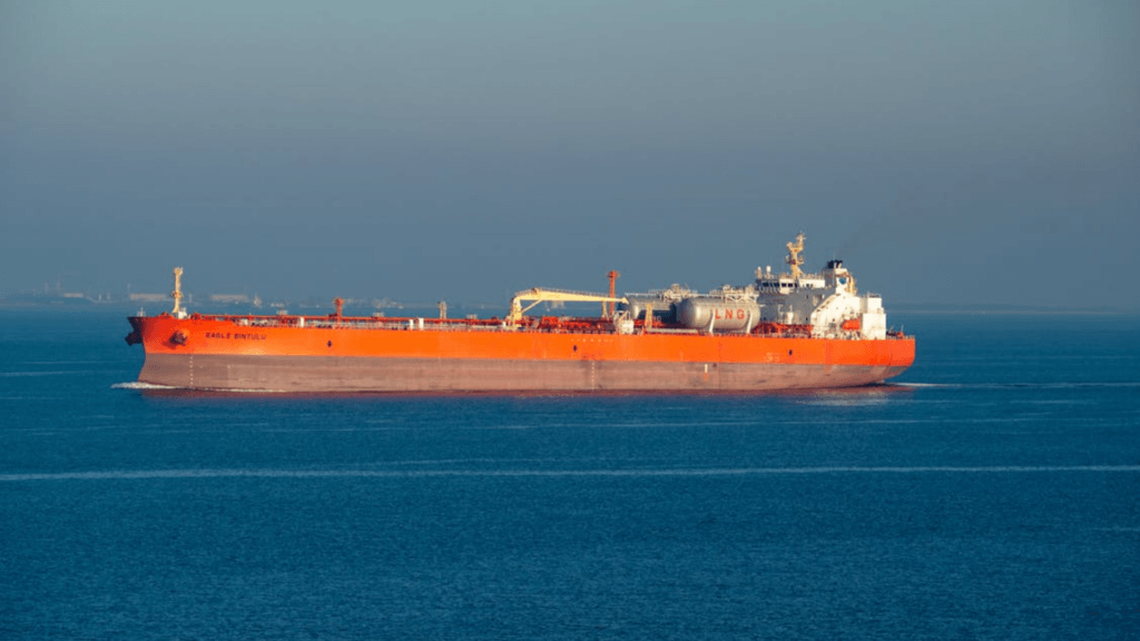 A large orange and grey oil tanker traveling across a calm blue sea under a clear sky.