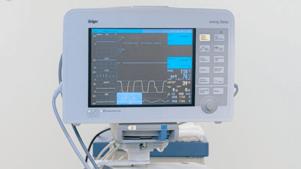 A medical patient monitor displaying vital signs such as heart rate and oxygen levels in a bright, clean hospital room.