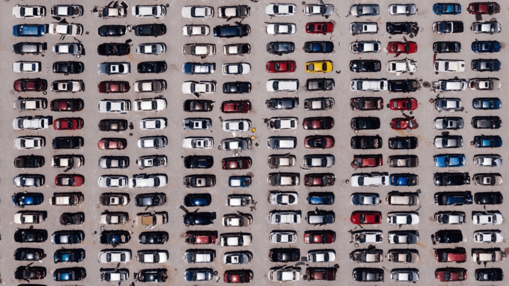 An overhead aerial view of a large parking lot or salvage yard filled with rows of various colored cars.