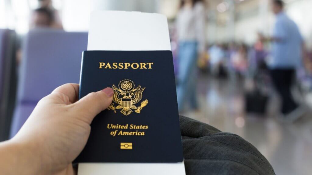 Traveler holding a passport and their luggage, as they check their smartphone at an airport.