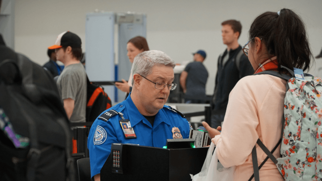 A TSA officer checking a passenger's boarding pass and identification at a security podium.