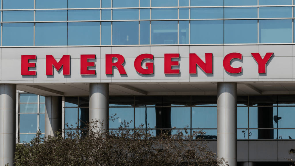 A large, red _EMERGENCY_ sign on the exterior of a modern glass hospital building.