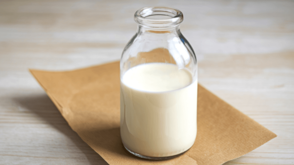 A small glass bottle filled with milk resting on a piece of brown paper.