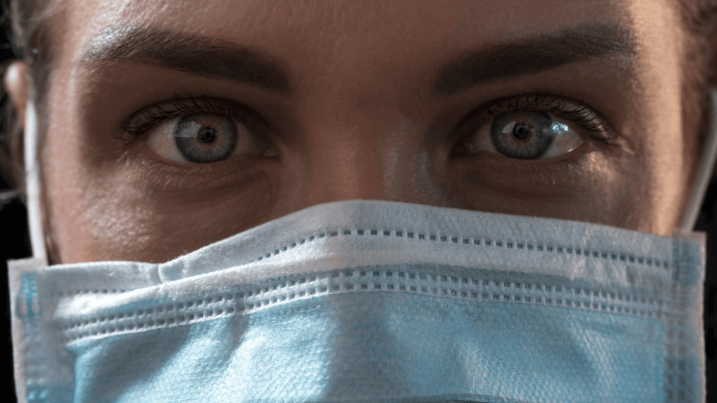 Extreme close-up of a person's eyes and forehead while wearing a blue disposable medical face mask.