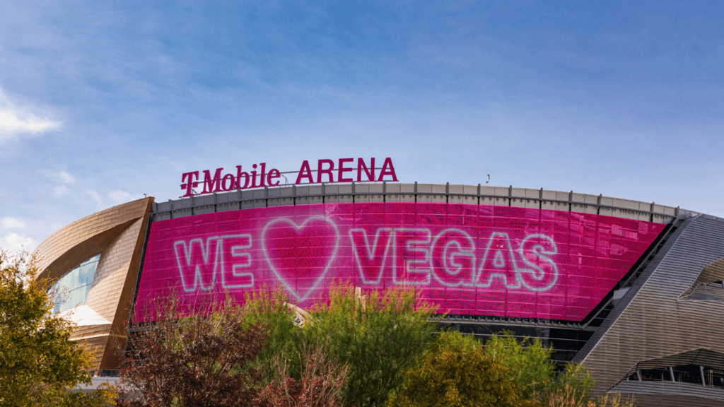 The exterior of T-Mobile Arena in Las Vegas, showing a large pink LED screen with the message _WE ❤️ VEGAS.