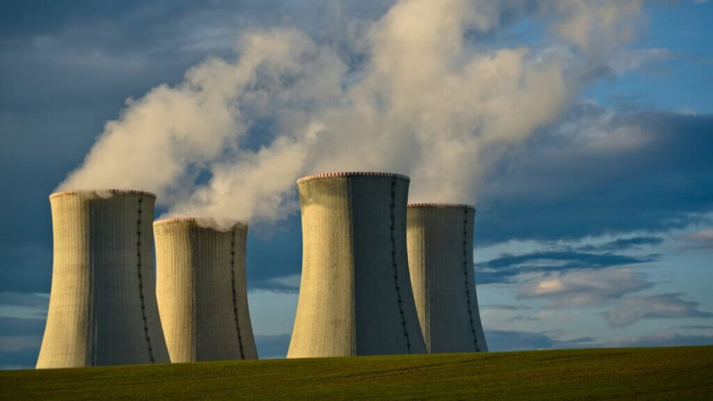 Nuclear power plant cooling towers releasing steam over an overcast sky.
