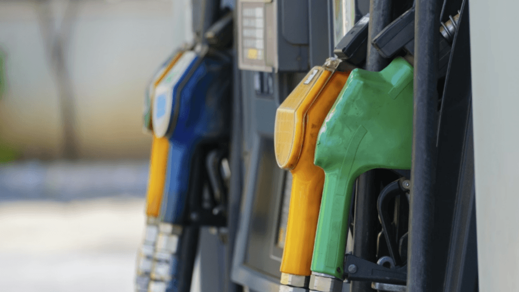 A row of colorful fuel nozzles (blue, orange, and green) hanging at a gas station pump.
