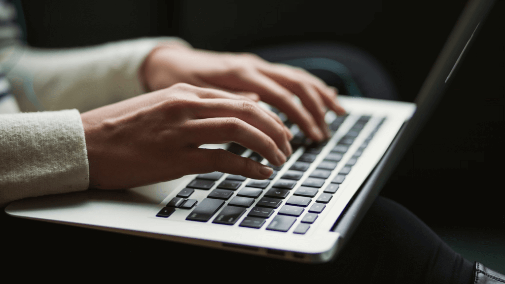 Close-up of a person's hands typing on a silver laptop keyboard.