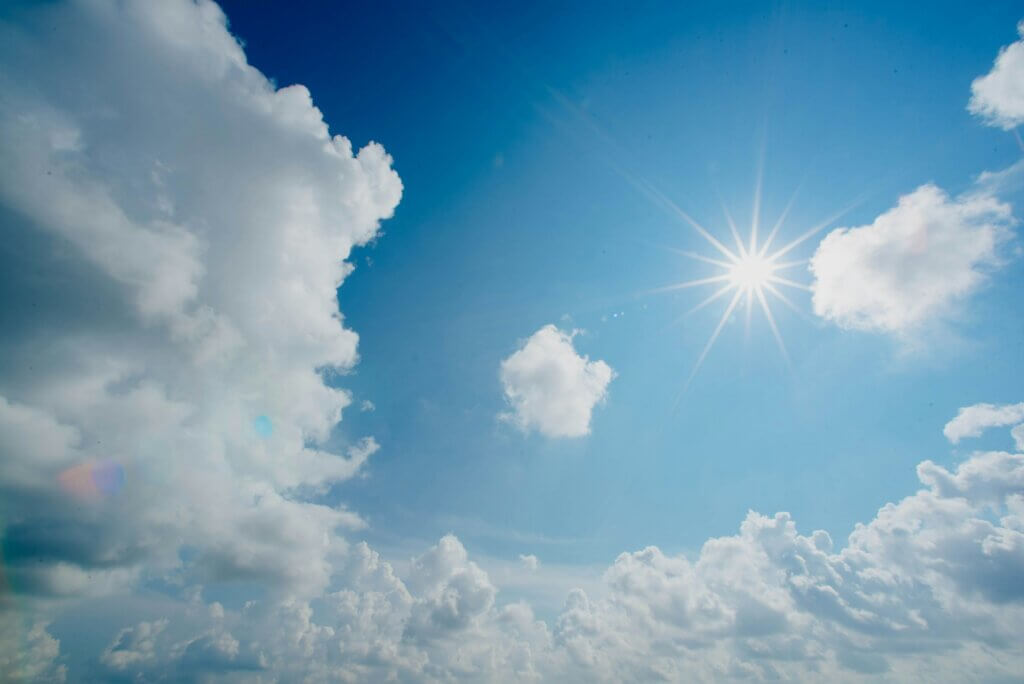 Bright sun shining in a blue sky with scattered white clouds on a clear day.