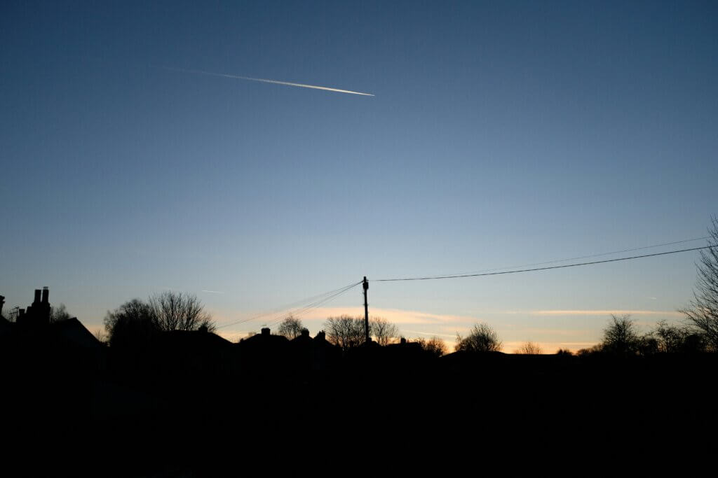 Silhouetted rooftops at sunset with a bright streak in the sky.