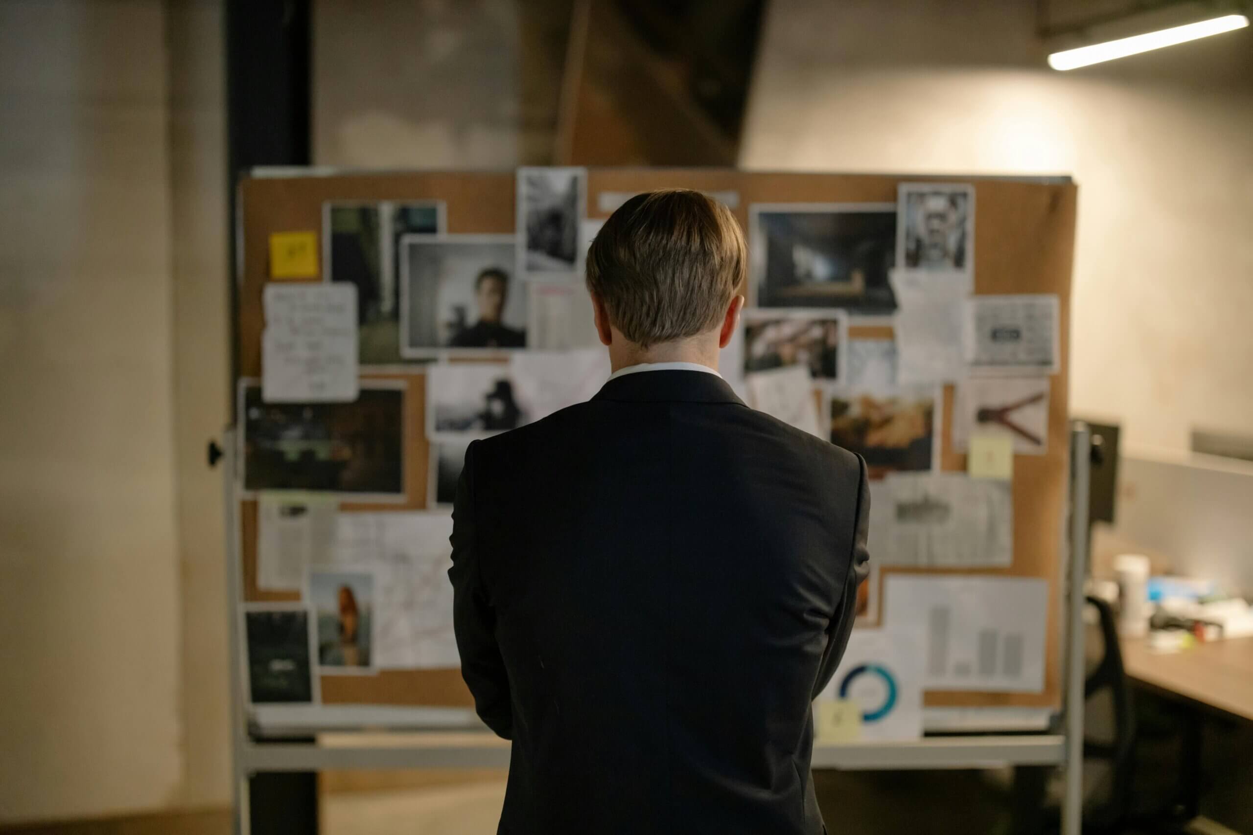 Man in suit examining photos and notes on investigation board.