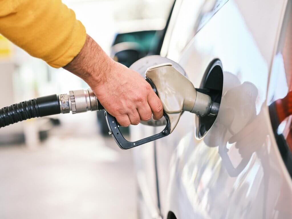 Person holding fuel pump nozzle while refueling a car at a gas station.