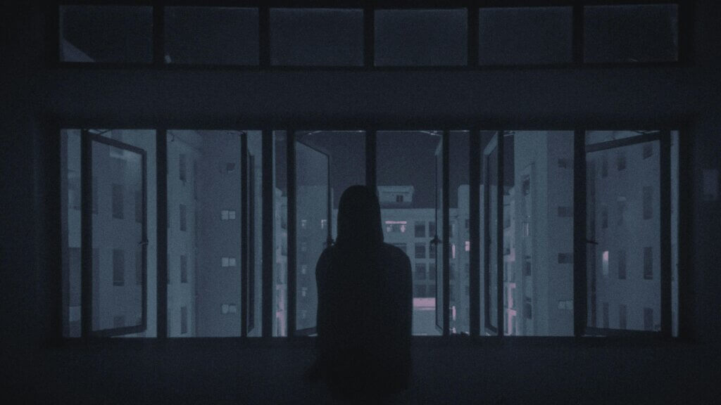 Silhouette of woman by window at night with somber mood and faint city lights.