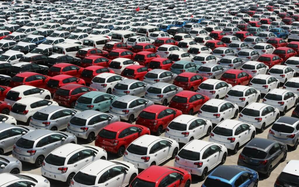 Large parking lot filled with rows of compact cars in red, white, and silver.