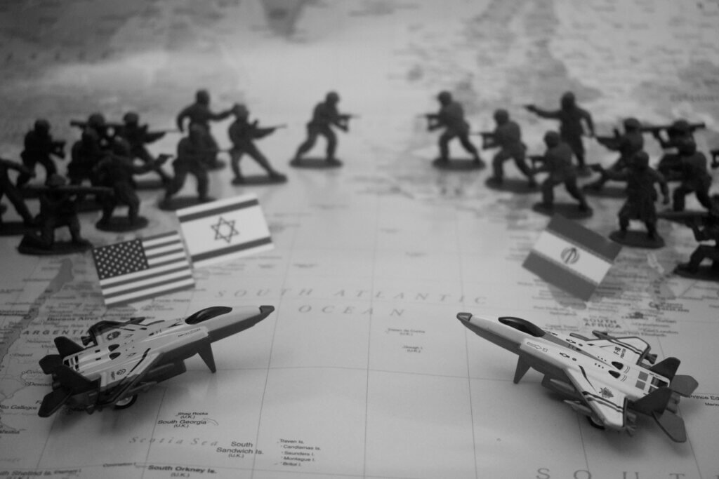 Toy soldiers and fighter jets positioned on a world map with U.S., Israel, and Iran flags representing geopolitical conflict.