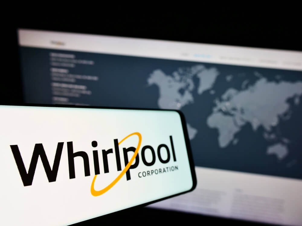 Whirlpool Corporation logo displayed on a smartphone screen with a world map on a computer monitor in the background.