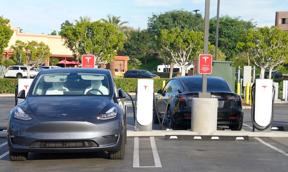 Electric vehicles parked at Supercharger station with charging units in a parking lot.