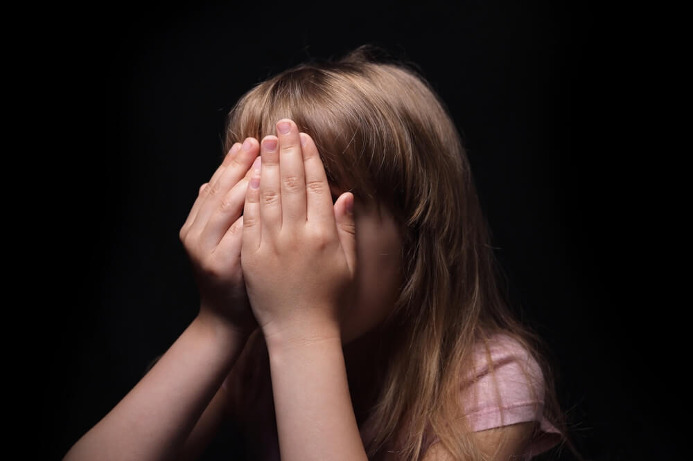 Young girl covering her face with hands while crying.