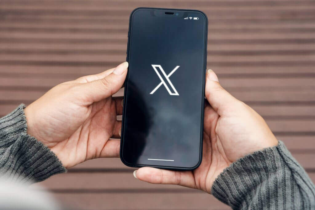 Smartphone displaying X logo held in both hands.