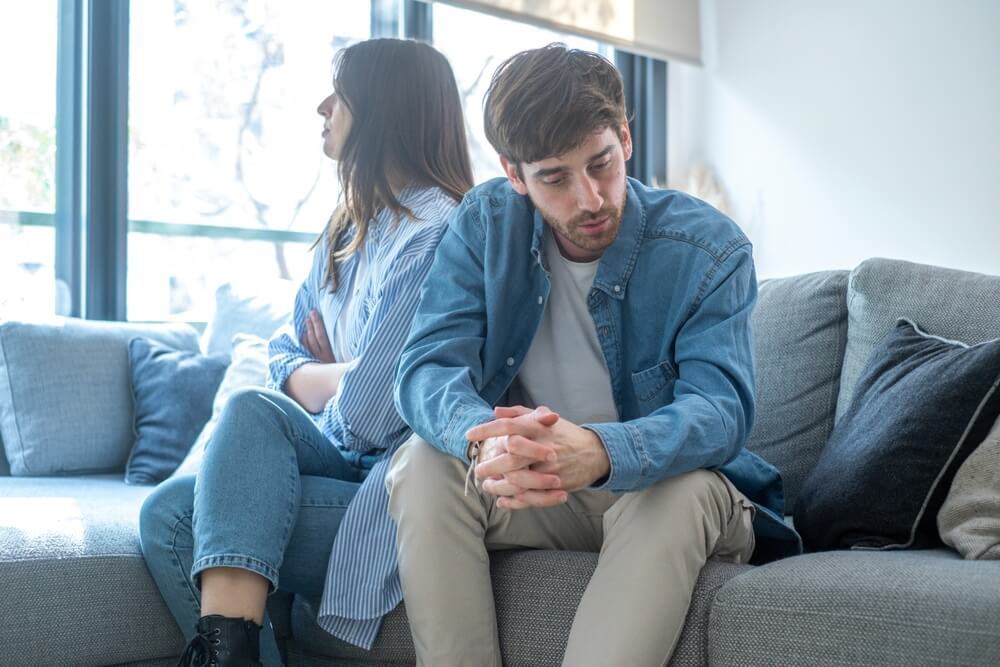 Couple sitting back-to-back on a couch during an argument.