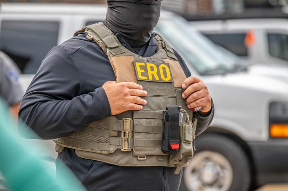 Masked ERO agent with hands in his tactical vest.