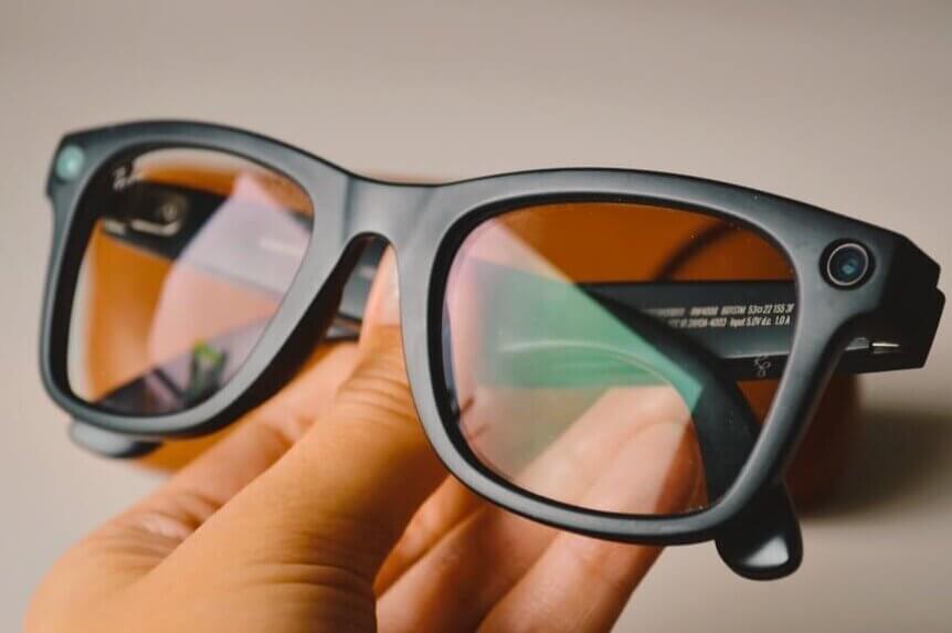 Ray-Ban Meta smart glasses with built-in camera lens on the frame displayed on a hand.