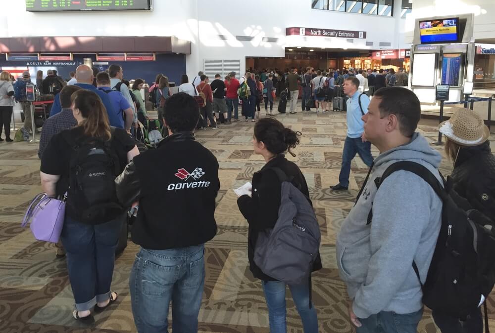 Passengers standing in a long line at an airport check-in counter with luggage and backpacks.