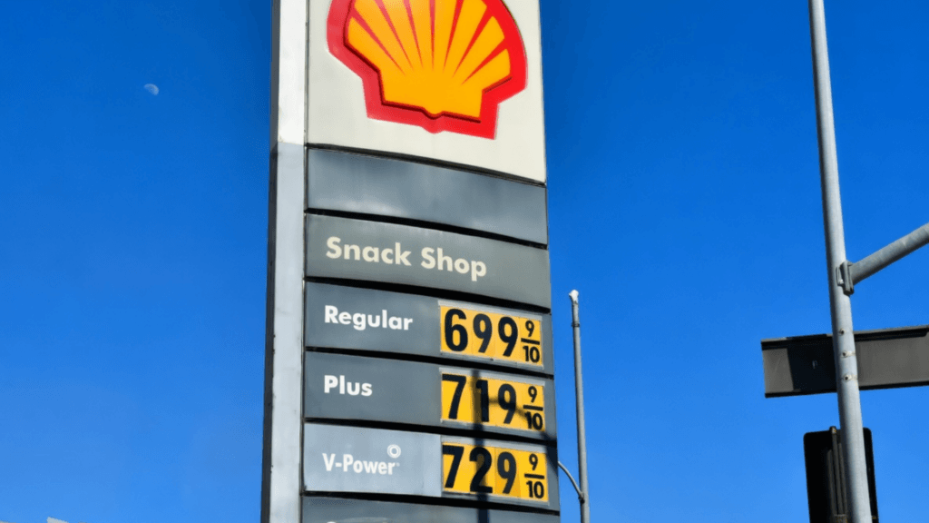 A tall Shell gas station sign against a bright blue sky showing high fuel prices.