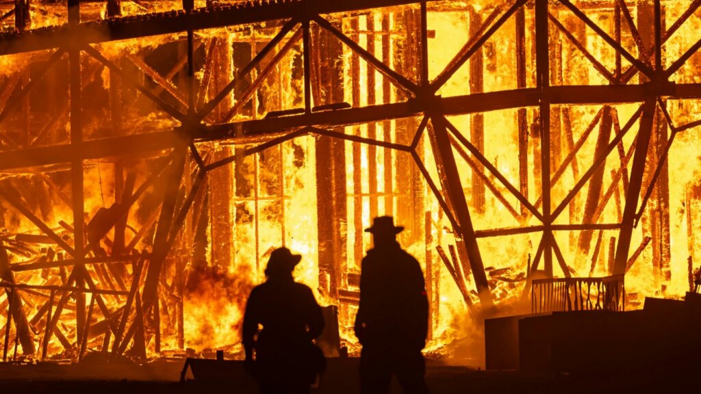 Silhouetted firefighters battling a large blaze inside an industrial structure.