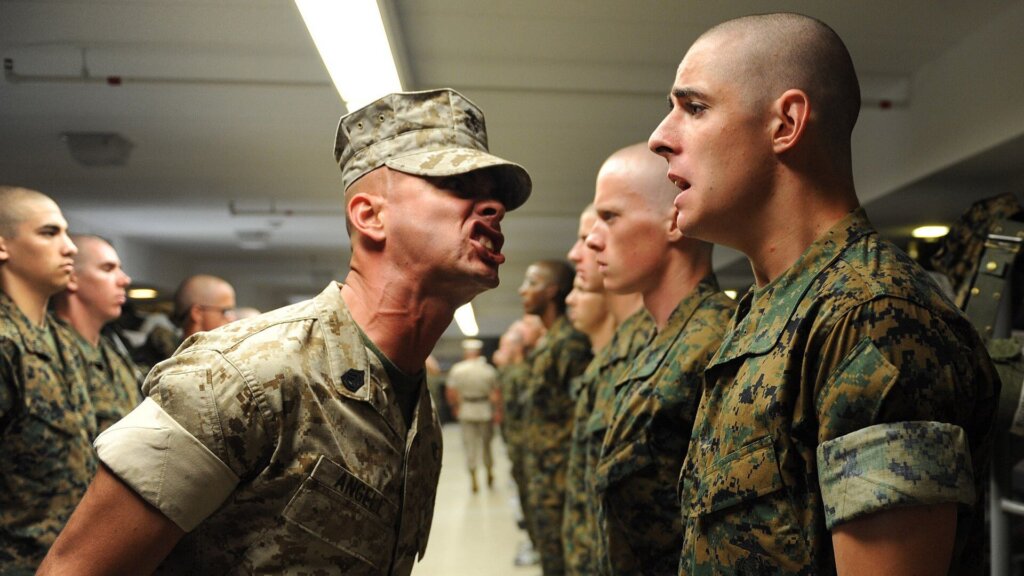 Drill instructor shouting at U.S. Marine recruits standing in formation during training.