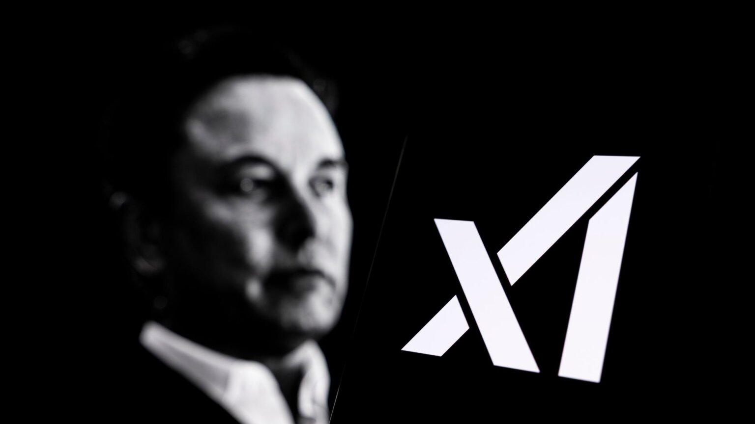 The logo of xAI, Elon Musk's artificial intelligence company, is displayed on a smartphone screen. A portrait of Elon Musk is visible in the background.